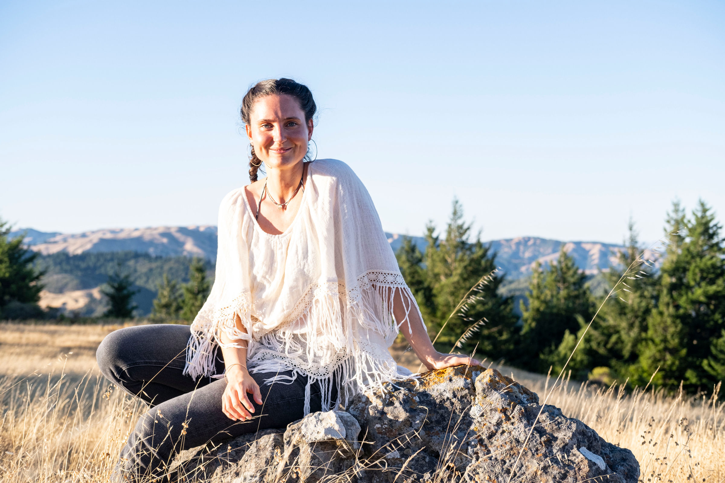 Coco Borsche seated on a rock in the golden hills of Marin County, California, smiling toward the camera